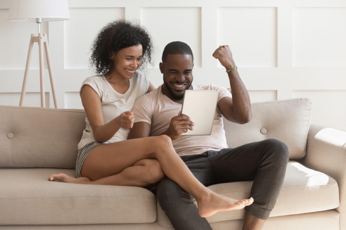 black couple online shopping excitedly while sitting on couch