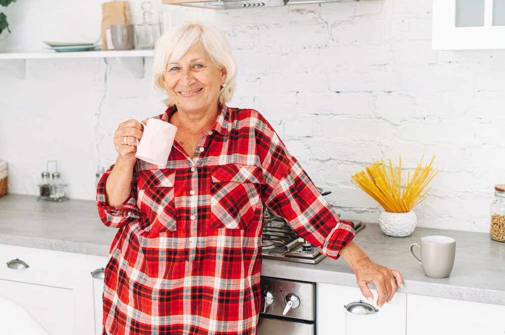 Happy smiling senior woman in kitchen at home with plaid flannel shirt and coffee mug