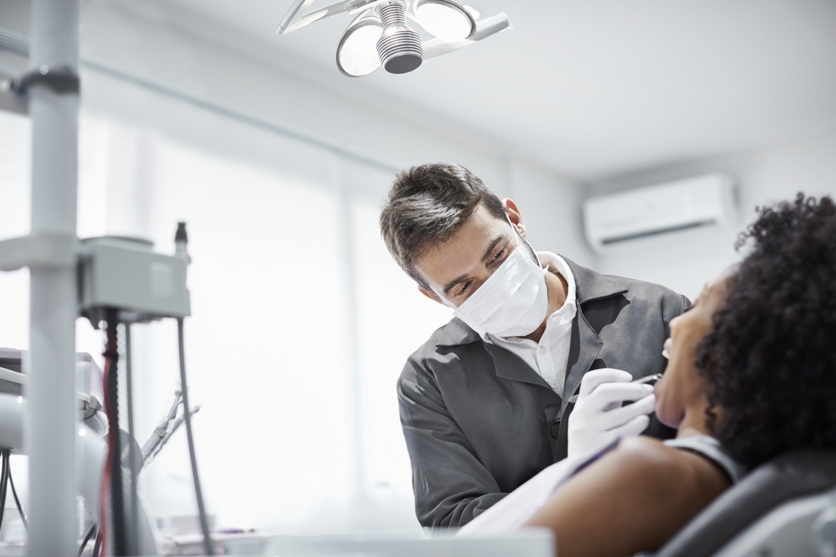 Male dentist examining teeth of patient on chair. Woman is visiting doctor for dental checkup. They are in clinic.