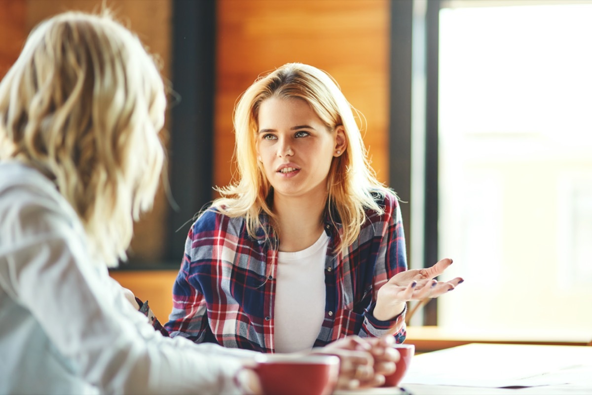 Two young female friends chatting over coffee in cafe.