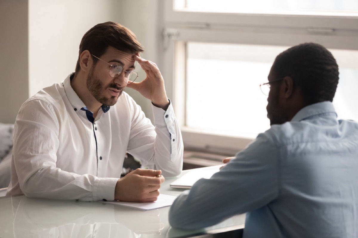 man holds head in hands while talking to another man