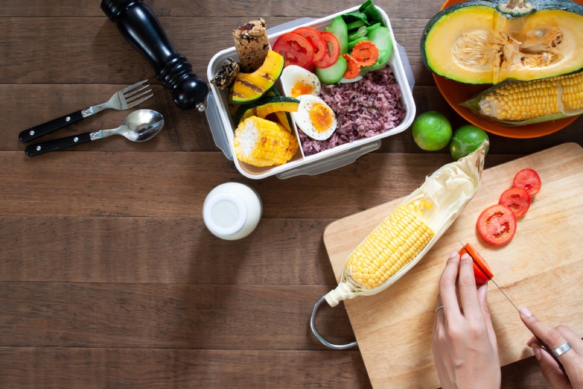 woman chopping tomatoes on cutting board with meal prep container in front of her, meal prep containers