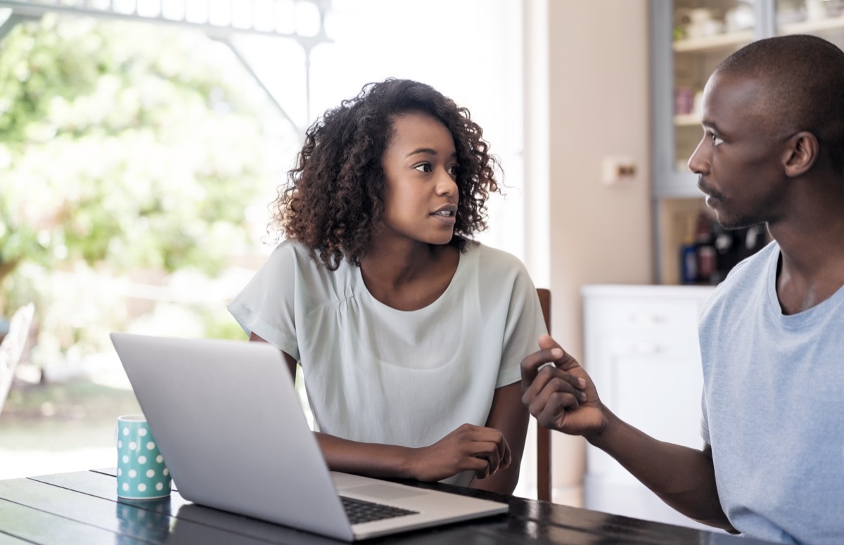 Serious young couple communicating at home. Laptop is on table. Woman is looking at man while discussing in room.