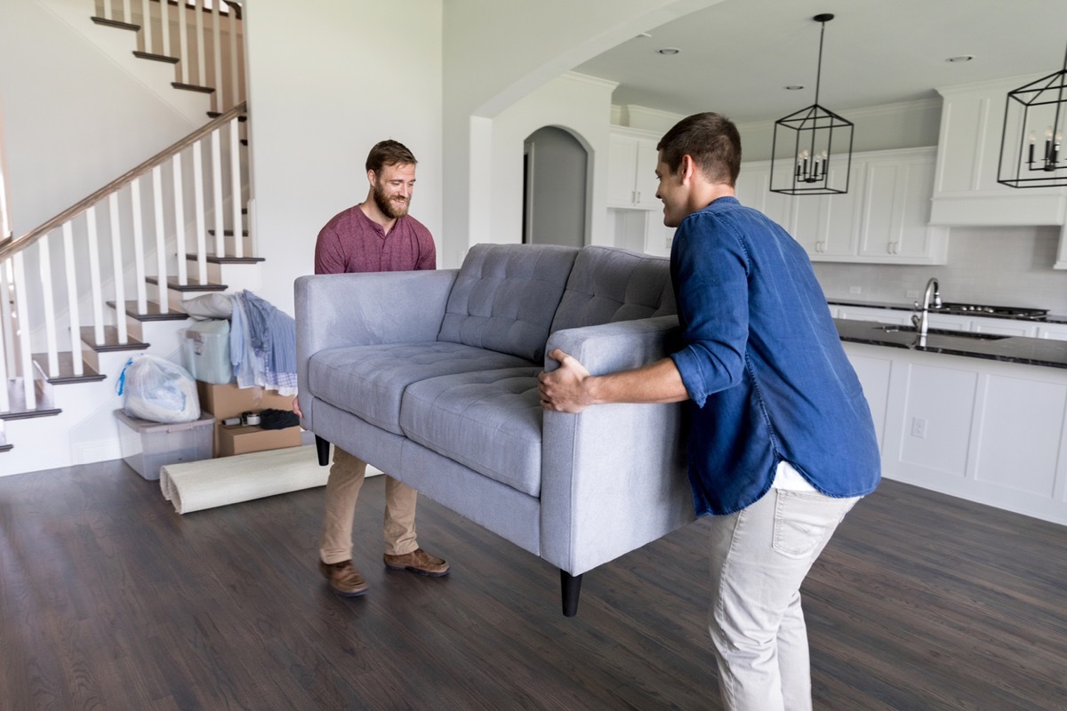 Young men work together to carry a sofa into a new home.