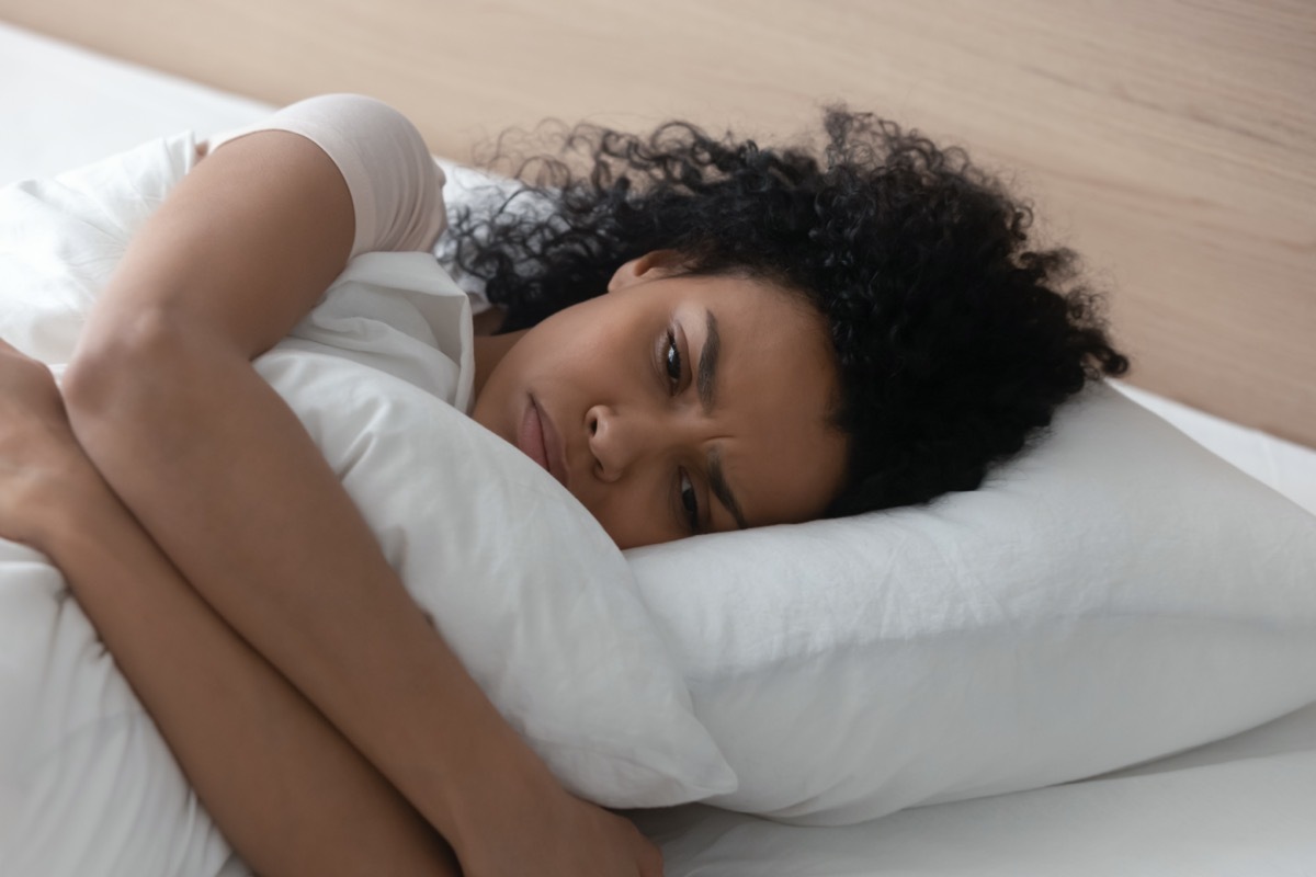 woman hugging pillow lying in bed alone