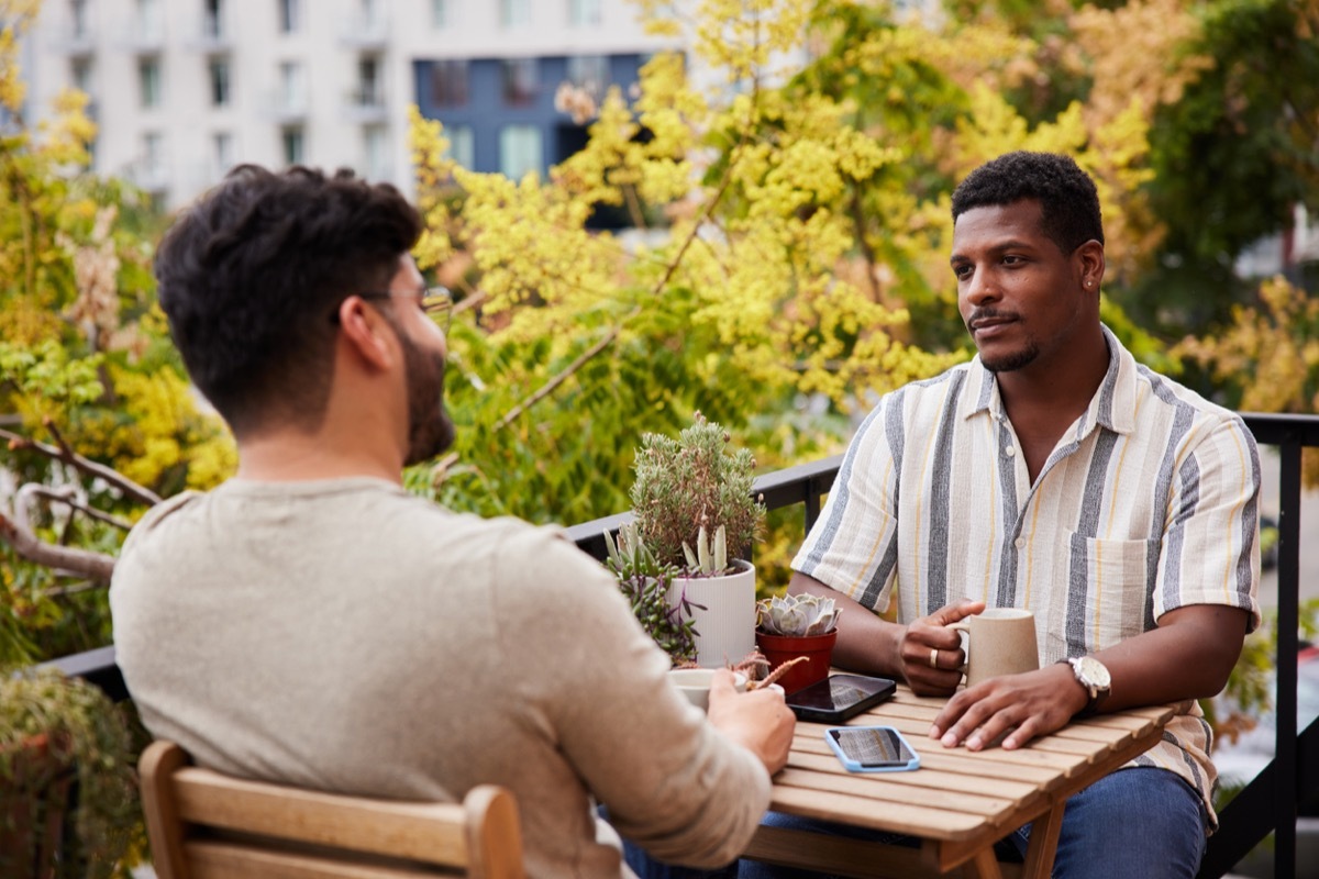 friends sitting on their apartment balcony in the city and talking over cups of coffee