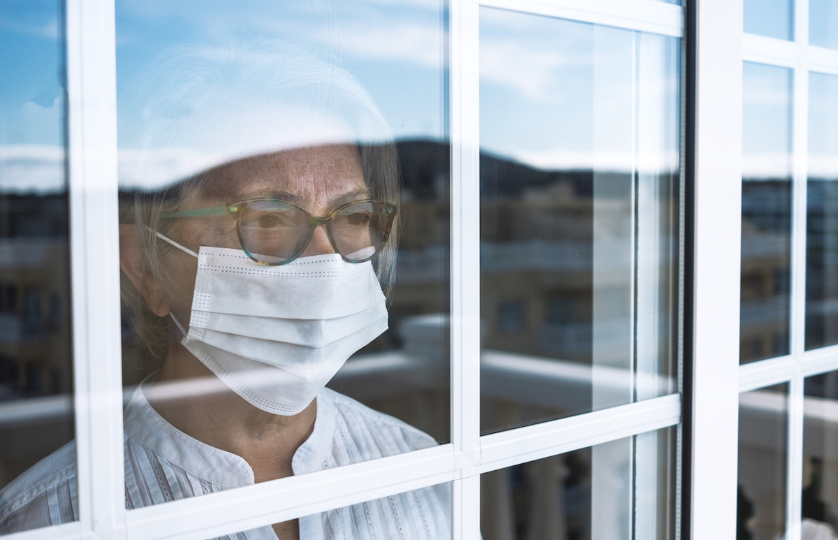 Senior woman in self quarantine to avoid contagion of infection by virus covid-19, stays home looking outdoors from the window